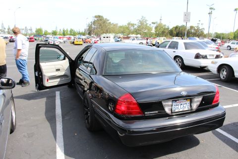 Rear three-quarter of black Ford sedan with door open and California plate 6GLC676 at car meet
