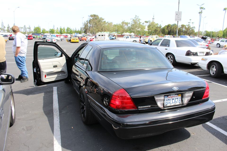 Rear three-quarter of black Ford sedan with door open and California plate 6GLC676 at car meet