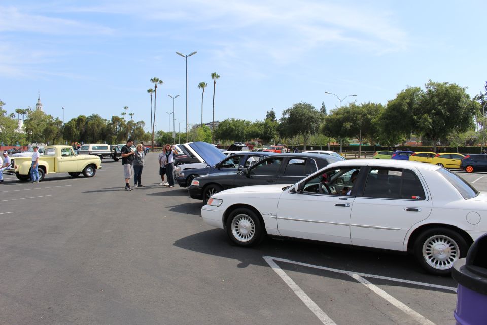 White full-size sedan and an older pickup truck in a parking-lot car meet with palm trees