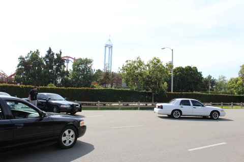 White and black sedans on lot roadway with amusement park drop tower behind