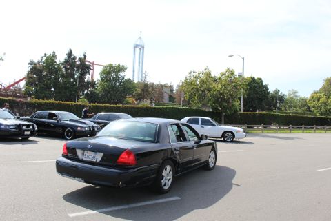 Rear view of a black sedan parked with a drop tower behind the trees