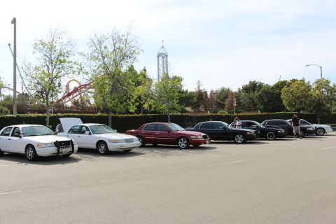 Lineup of sedans, one with hood open, beside amusement park rides