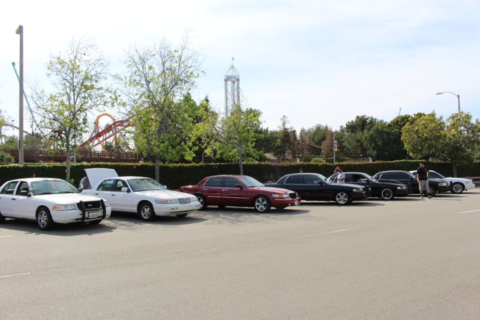 Lineup of sedans, one with hood open, beside amusement park rides