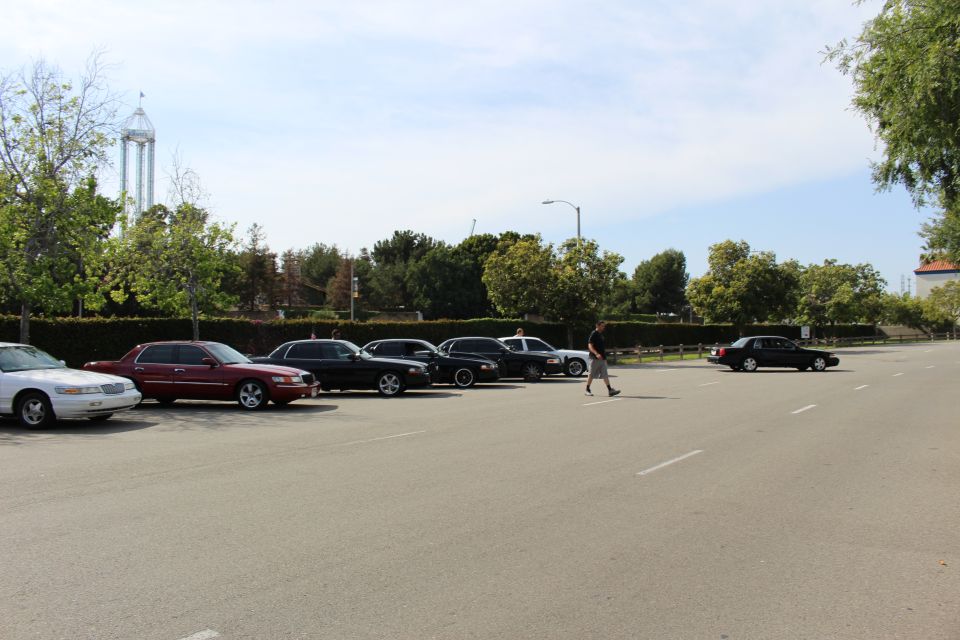 Person walking across a lot past parked white, maroon and black sedans