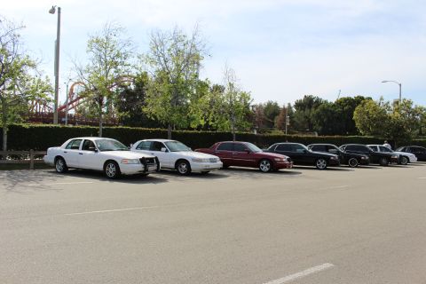 Front-angle view of parked sedans beside a hedge and roller coaster