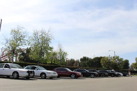 Diagonal view down a row of parked sedans with a coaster in the distance