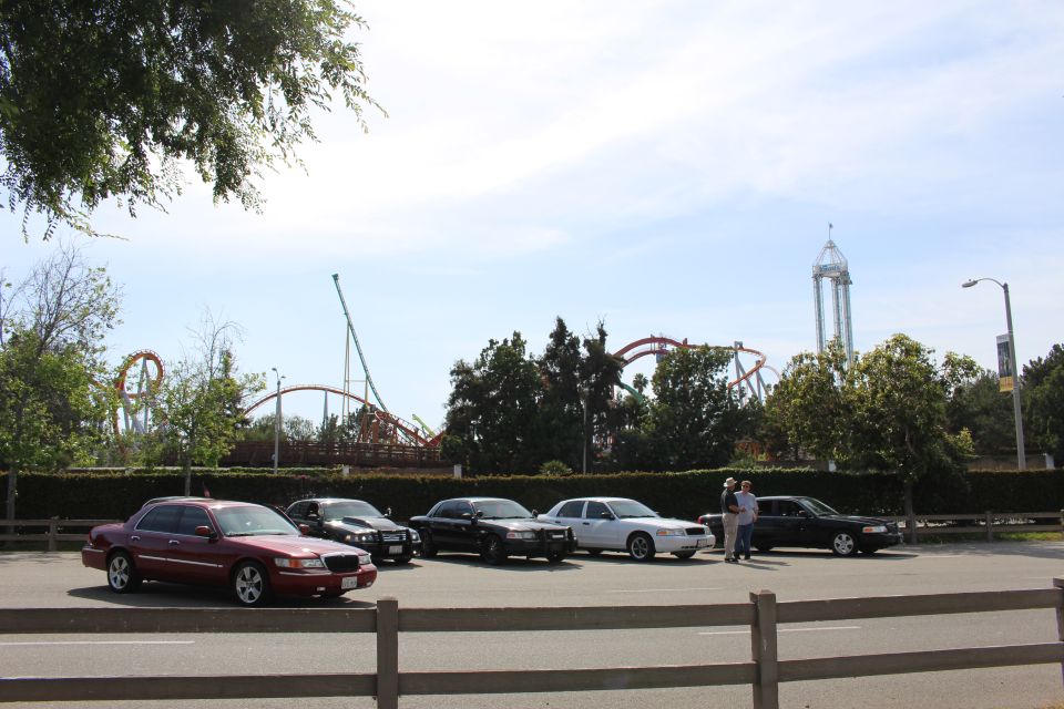 Five sedans parked in front of a fence with roller coasters behind