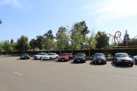Sedans parked across a lot with a tall red roller coaster behind