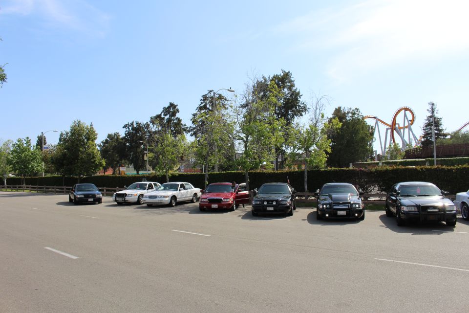 Sedans parked across a lot with a tall red roller coaster behind