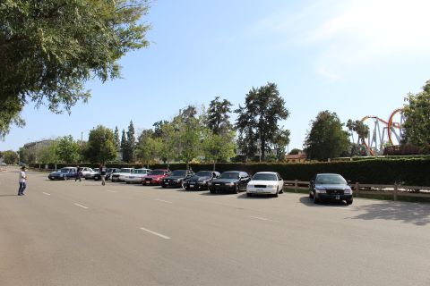 Person walking across a paved lot with parked sedans behind
