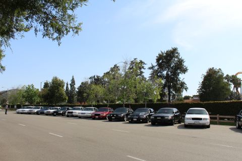 Line of parked sedans along a lot under a partly cloudy sky