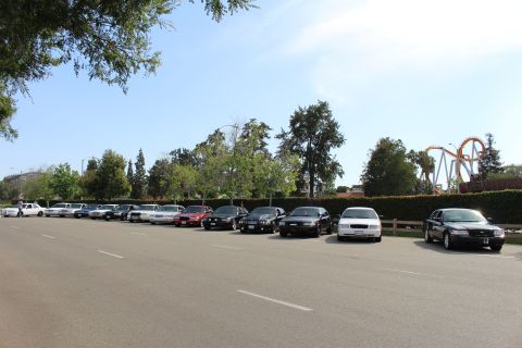 Parked sedans along a lot with a roller coaster behind