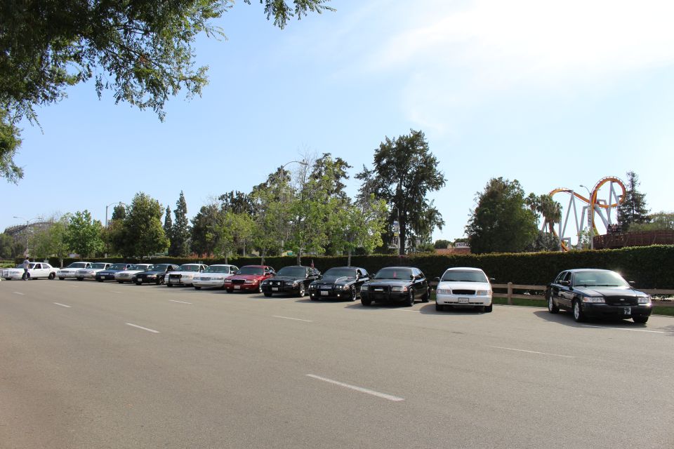 Parked sedans along a lot with a roller coaster behind