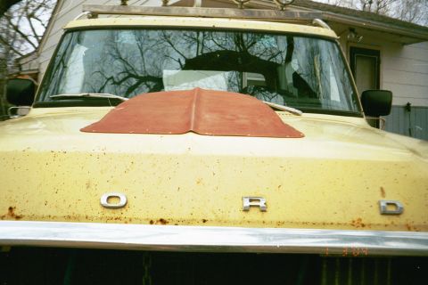 1979 Ford Bronco - Head-on view down the yellow hood of an older Ford truck showing raised chrome F-O-R-D letters across the leading edge and heavy rust speck…