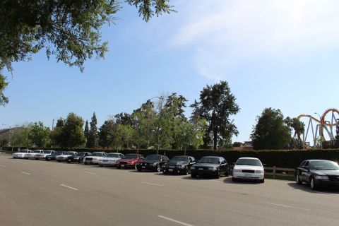Diagonal line of parked sedans with roller coaster behind