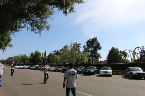 People walking across a lot with parked sedans and a coaster