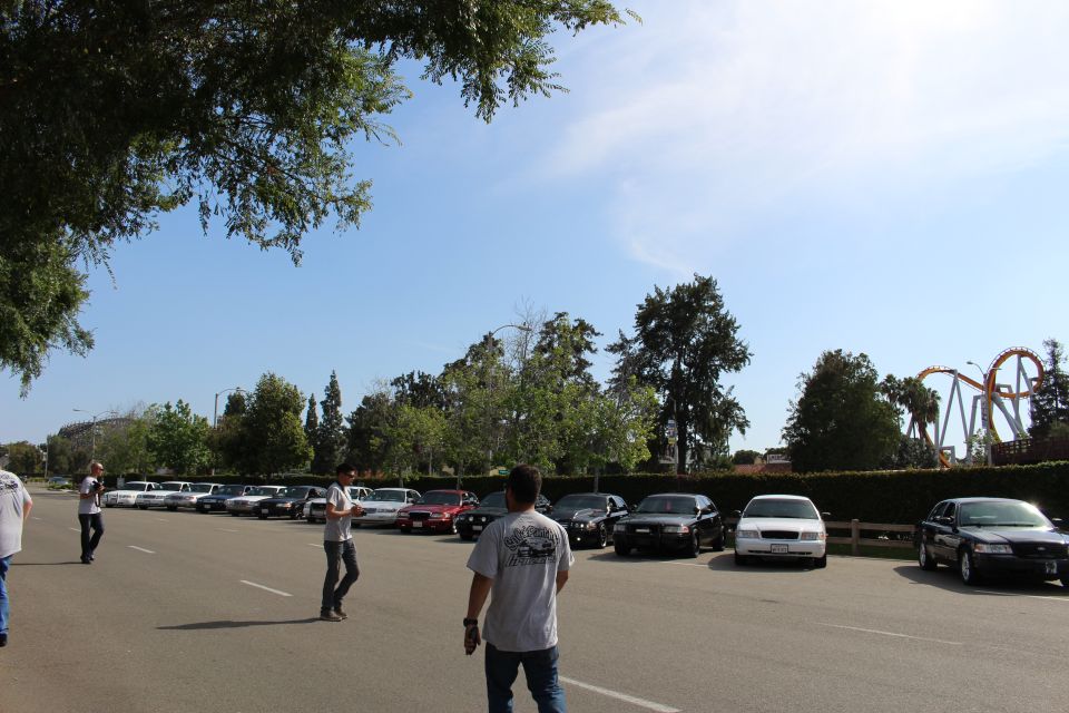 People walking across a lot with parked sedans and a coaster