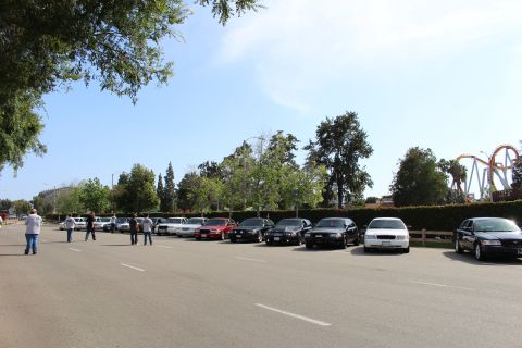 People walking in a lot beside a row of parked sedans