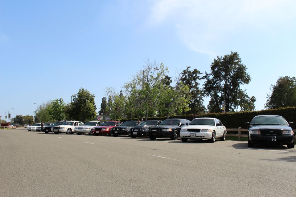 Row of parked sedans across a wide paved lot bordered by hedges and trees