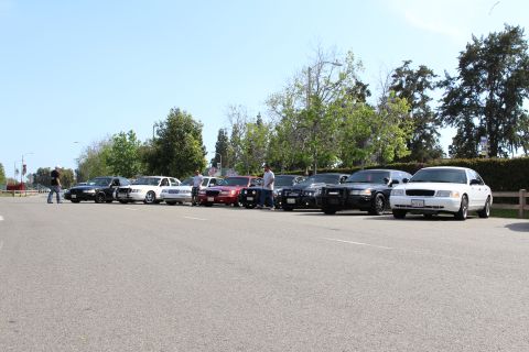 Front view of a row of parked cars including white and black sedans with people nearby