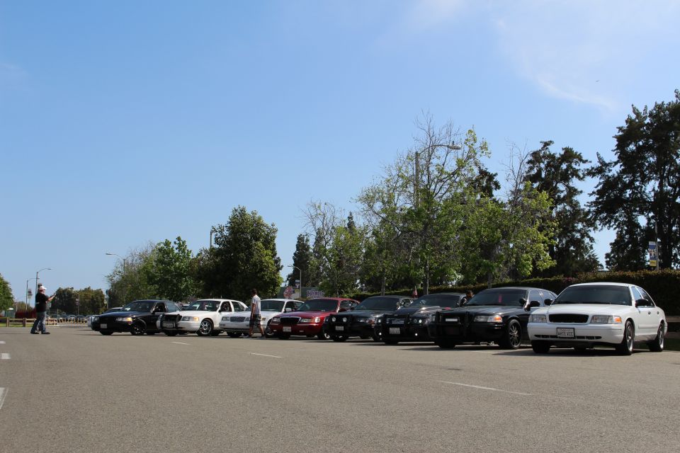 Row of sedans parked across a sunny paved lot with a person walking at left