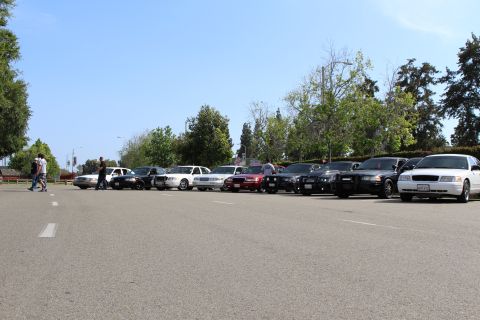 Row of parked sedans across a wide paved lot with pedestrians crossing at left