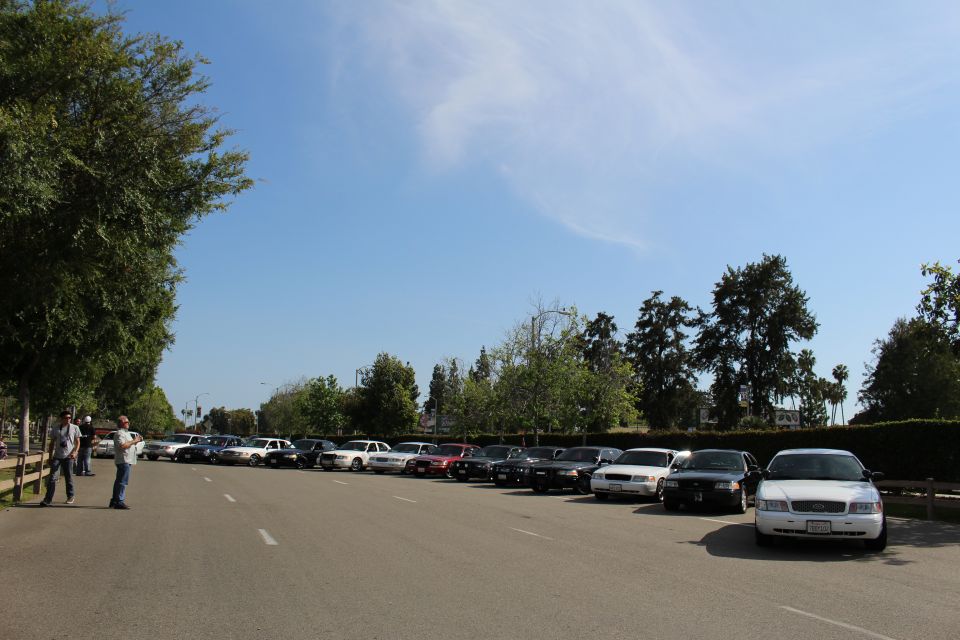 Row of parked vehicles across a paved lot with two men standing at left