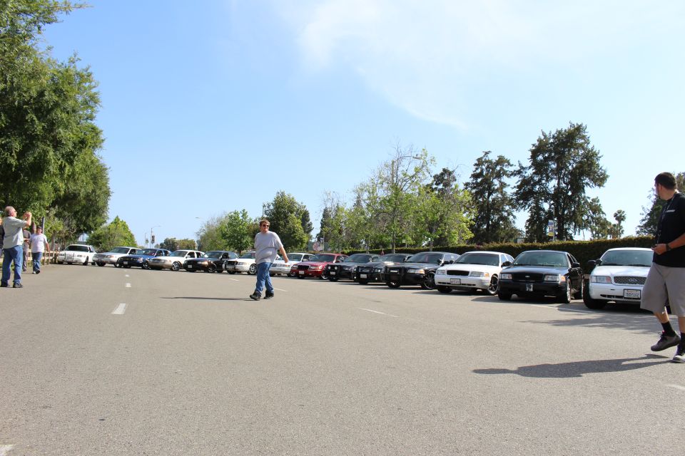 Wide paved lot with parked cars and several people walking, one in foreground right