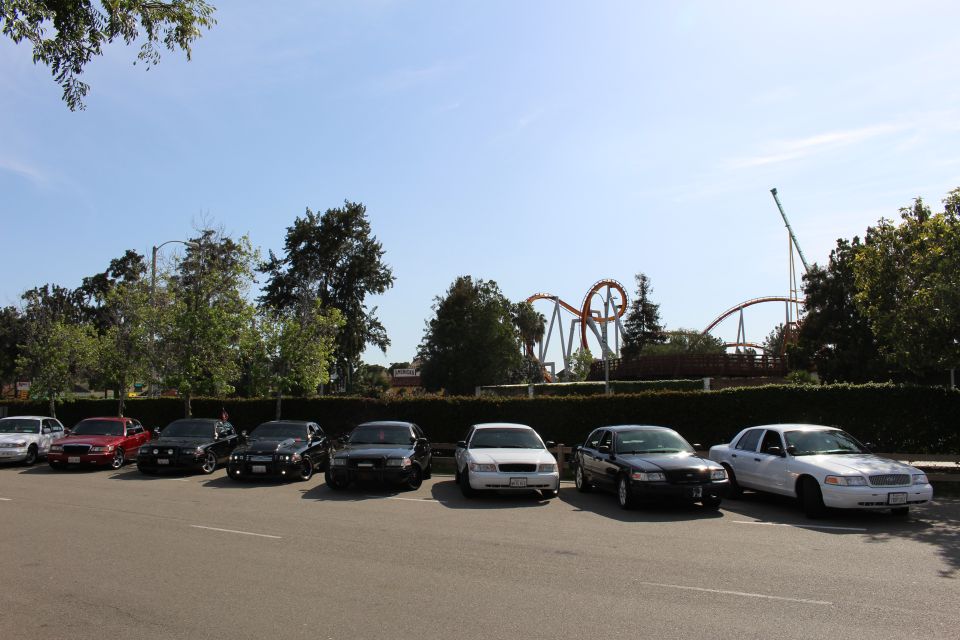 Row of parked cars in a lot with an amusement park roller coaster behind