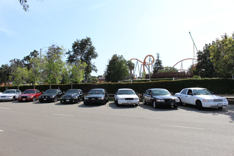 Row of full-size sedans parked in a lot with a roller coaster in the background