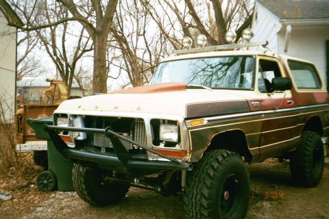 1979 Ford Bronco - This modified Ford Bronco is parked outdoors next to a house and some trees.