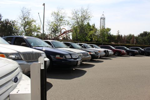 Front corners of a row of parked sedans and an SUV with a roller coaster behind