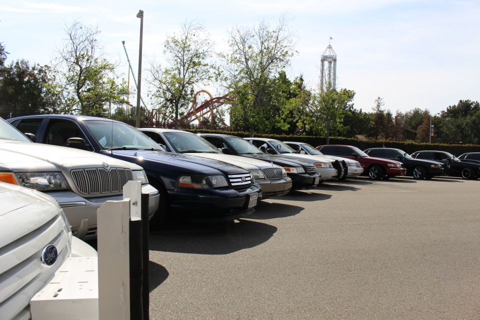 Front corners of a row of parked sedans and an SUV with a roller coaster behind