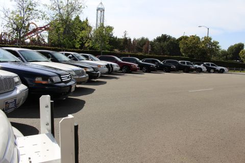 Row of parked sedans receding toward a tower ride in a parking lot