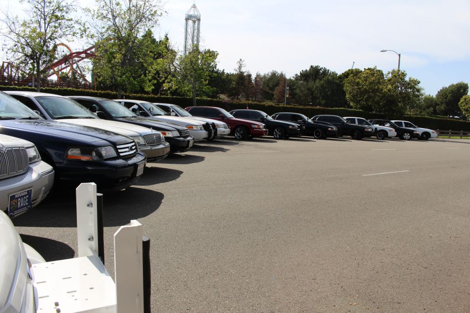 Row of parked sedans receding toward a tower ride in a parking lot
