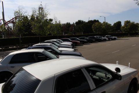 White sedan roofs in the foreground with a row of parked cars and a tower ride