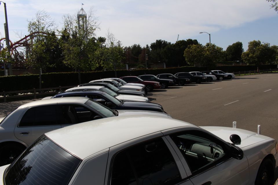 White sedan roofs in the foreground with a row of parked cars and a tower ride