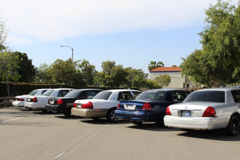 Rear three-quarter row of full-size sedans parked near a tiled-roof building