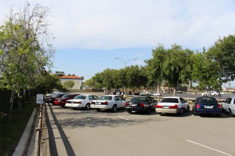 Parked sedans beside a 10 mph speed sign with people gathered in the background