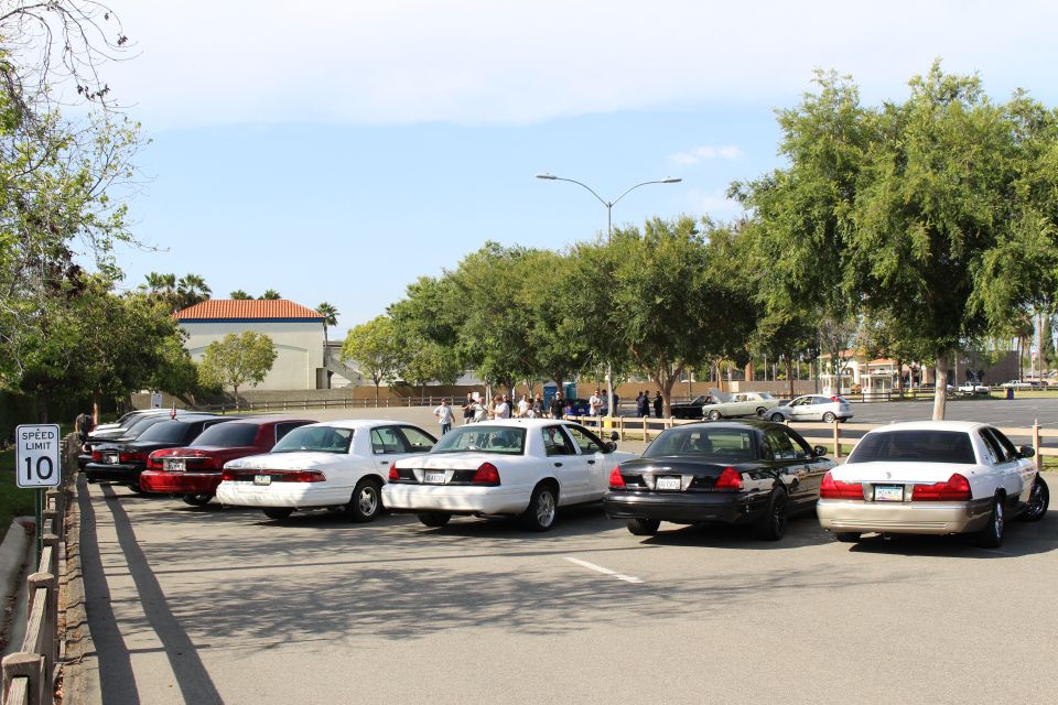 Diagonal row of sedans parked by a 10 mph sign with people gathered behind