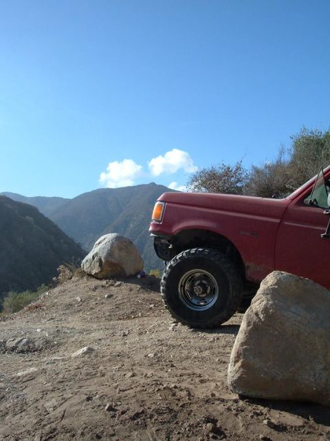 1988 Ford Bronco - A red truck is parked on a rocky incline with mountains in the background.