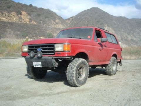 1988 Ford Bronco - This red Ford Bronco is equipped with off-road tires and auxiliary lights, ready for adventure in a , mountainous terrain.