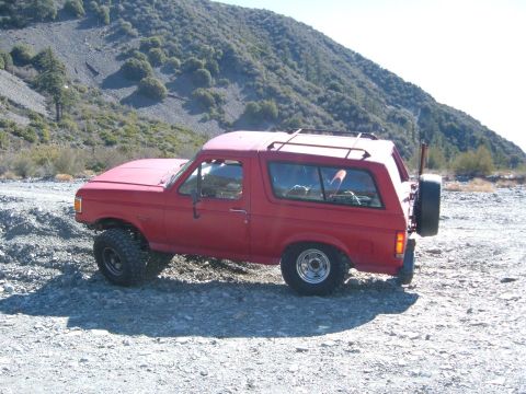 1988 Ford Bronco - A red SUV is parked on a rocky terrain with a mountain range behind it.