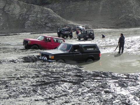 1988 Ford Bronco - A black 1988 Ford Bronco navigates a muddy obstacle course alongside other off-road vehicles.