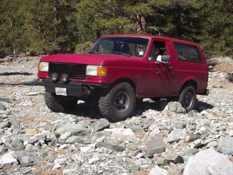 1988 Ford Bronco - Red 1987 Ford Bronco navigating a rocky off-road path with trees in the background.