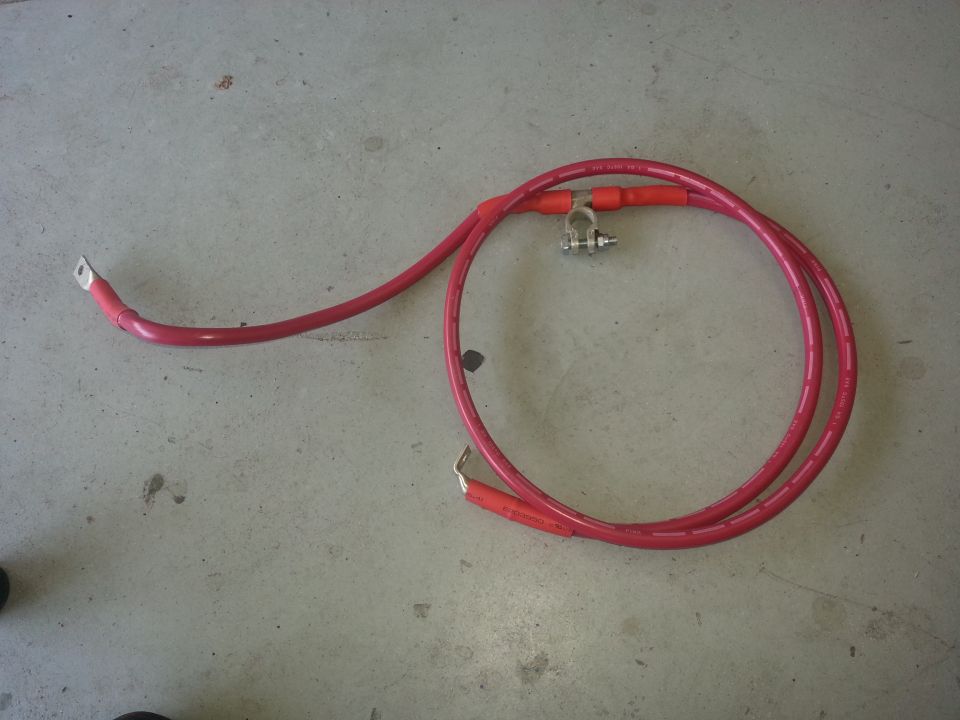 Red battery cables with metal terminals and a clamp, lying on a concrete floor