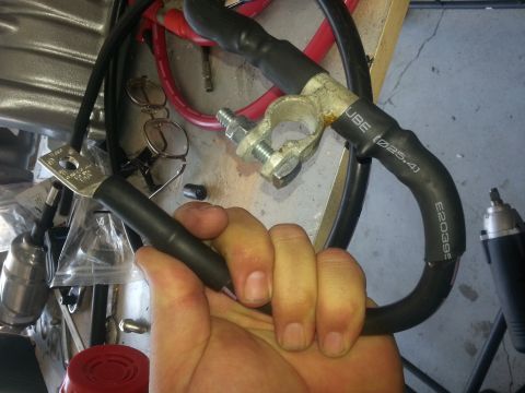 1994 Ford Bronco - A close-up shows a battery cable with a clamp and visible part numbers, held by a hand.