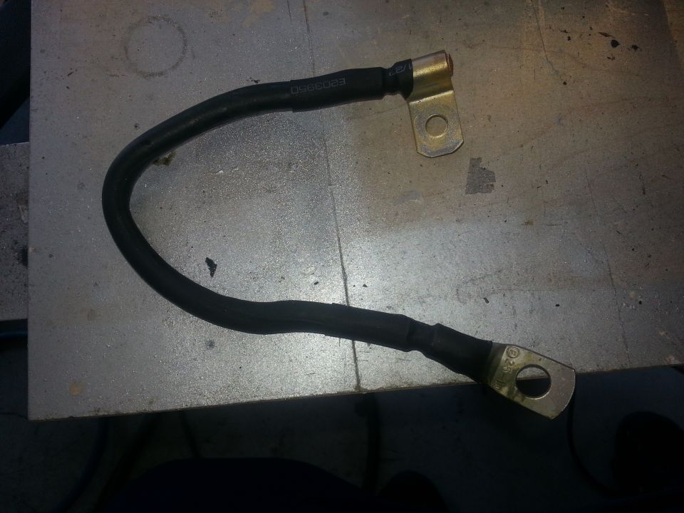 Battery cable with metal terminals on a metallic surface. Text reads "DW2023"