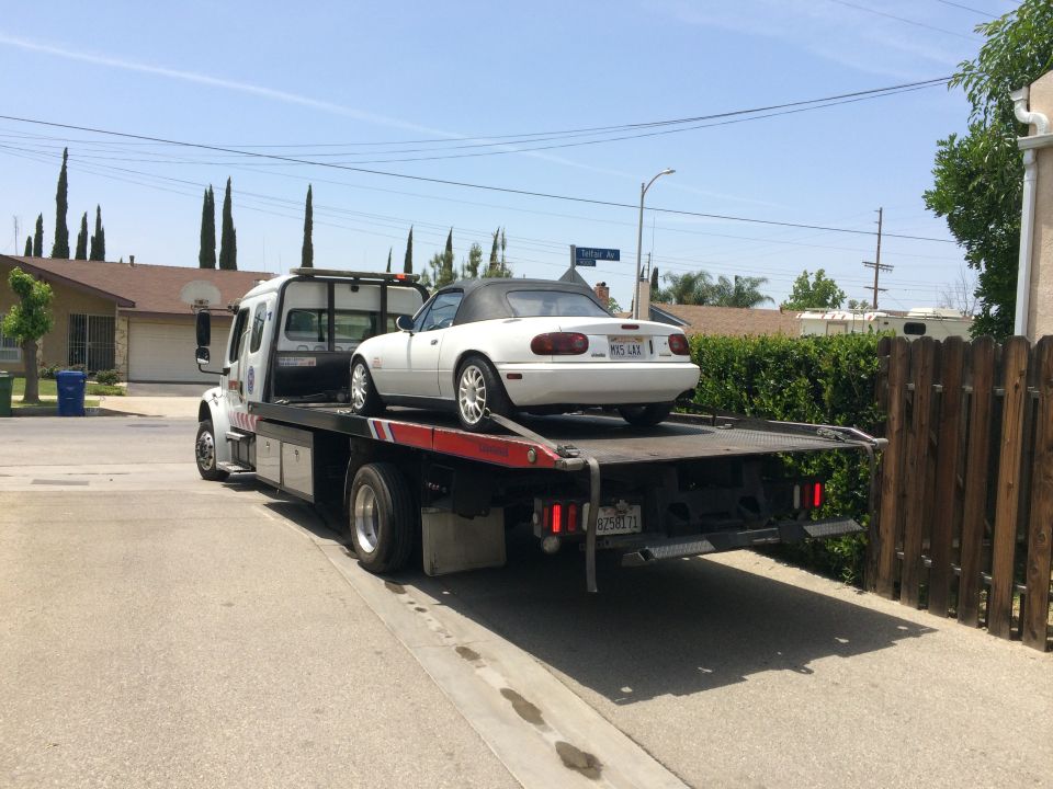 White convertible sports car on a flatbed tow truck, rear view