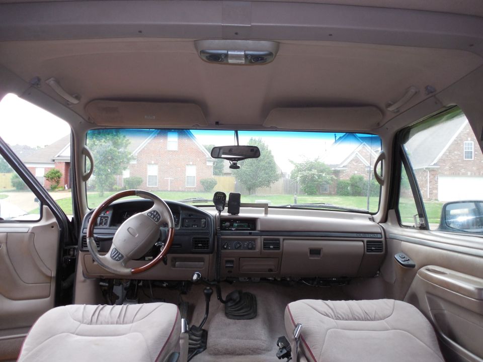 Tan interior of a Ford truck showing dash, wood-rim wheel, and CB radio, viewed from rear seat.